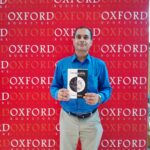 Somik holding a hardcover copy of Invaluable with a backdrop of Oxford Bookstore