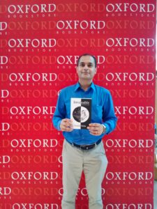 Somik holding a hardcover copy of Invaluable with a backdrop of Oxford Bookstore